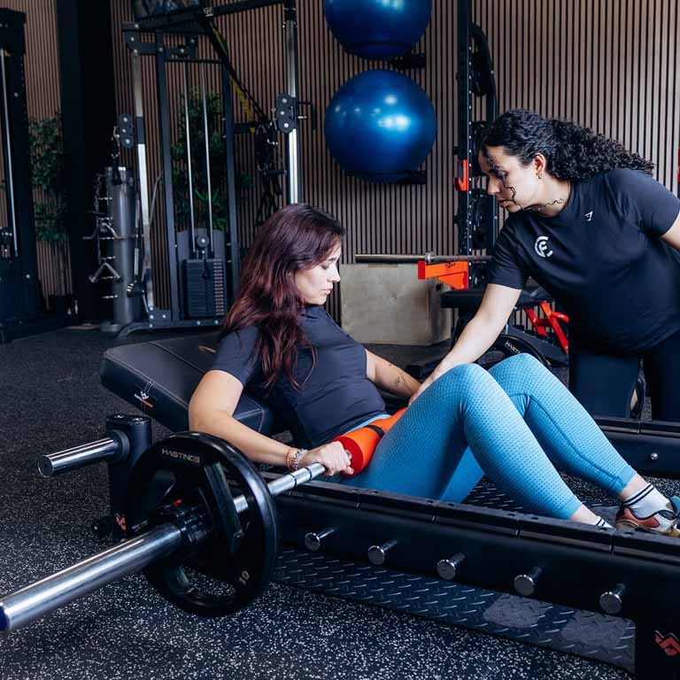 personal training mevrouw doet zittende oefening met een halter onder toezicht van een personal trainer